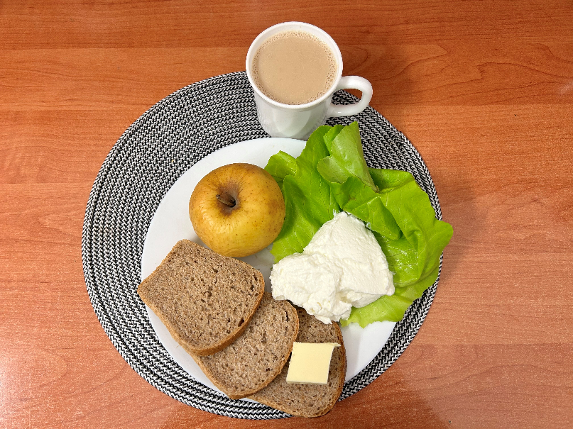 Na zdjęciu znajduje się: Kawa z mlekiem, Chleb Graham, Masło extra 82%, Serek homo. naturalny, Jabłko pieczone, ​​​​​​​Sałata zielona
